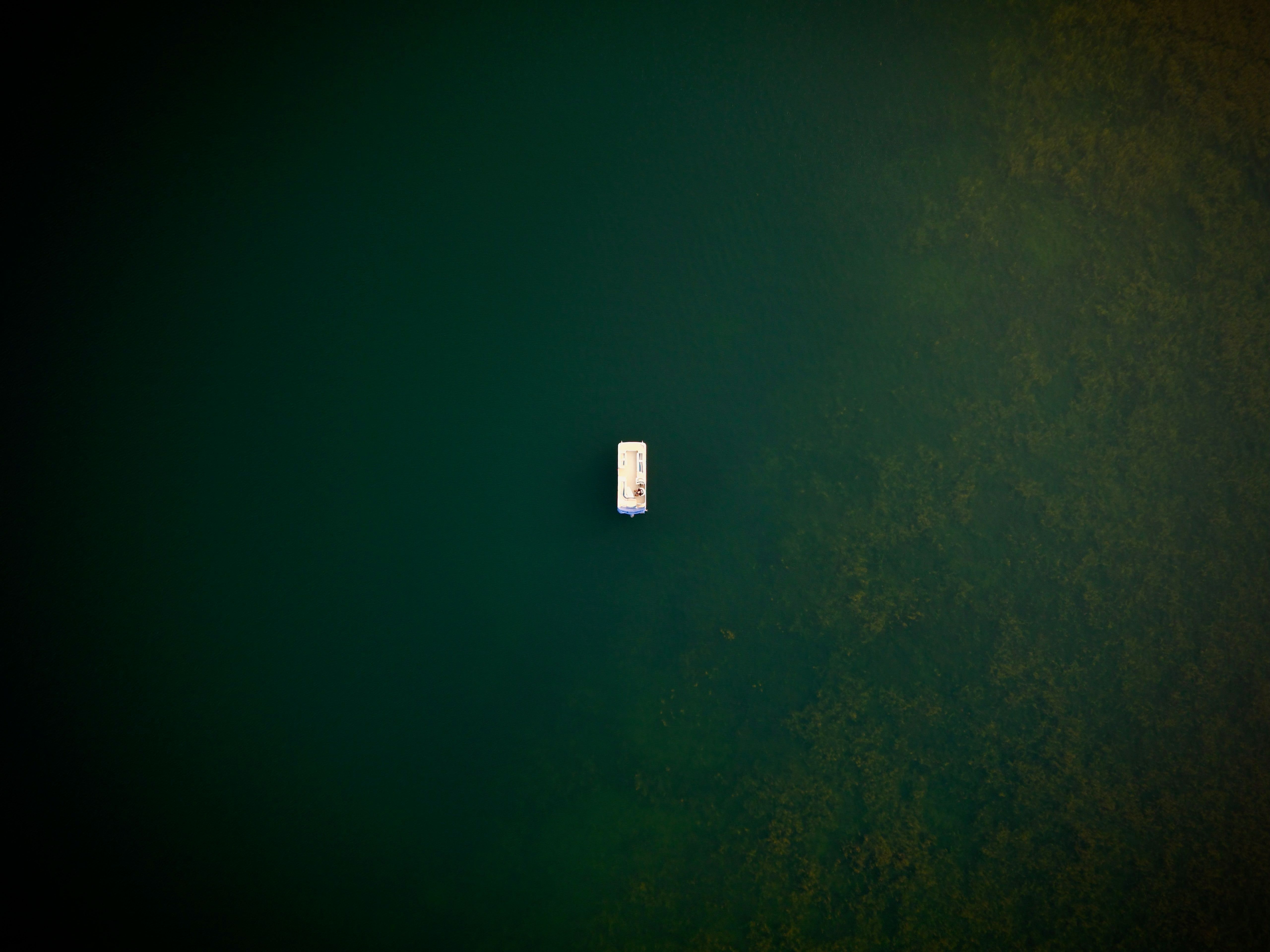 A small boat alone on deep green water, seen from directly above