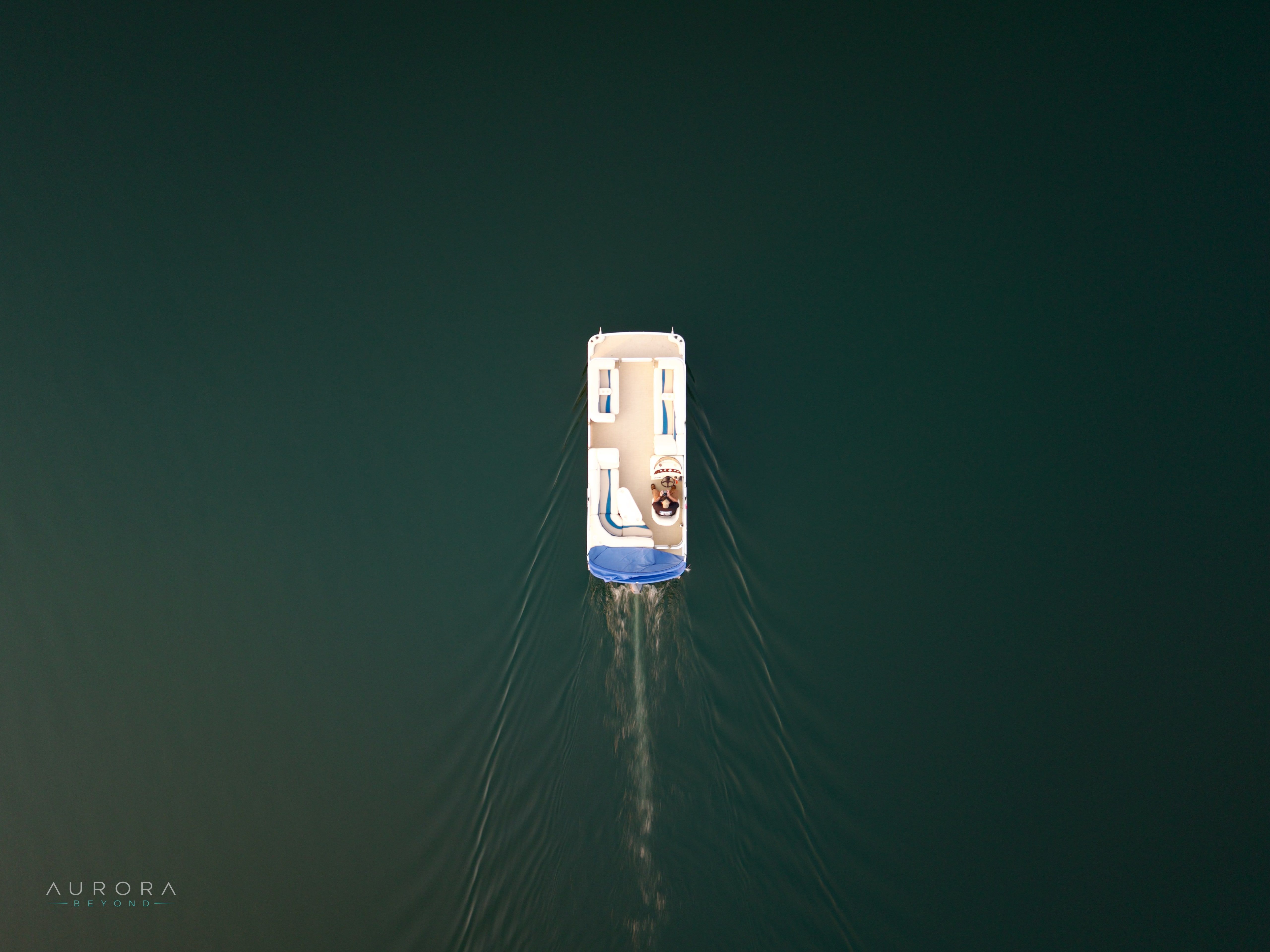 A pontoon boat crossing teal water, wake trailing behind it