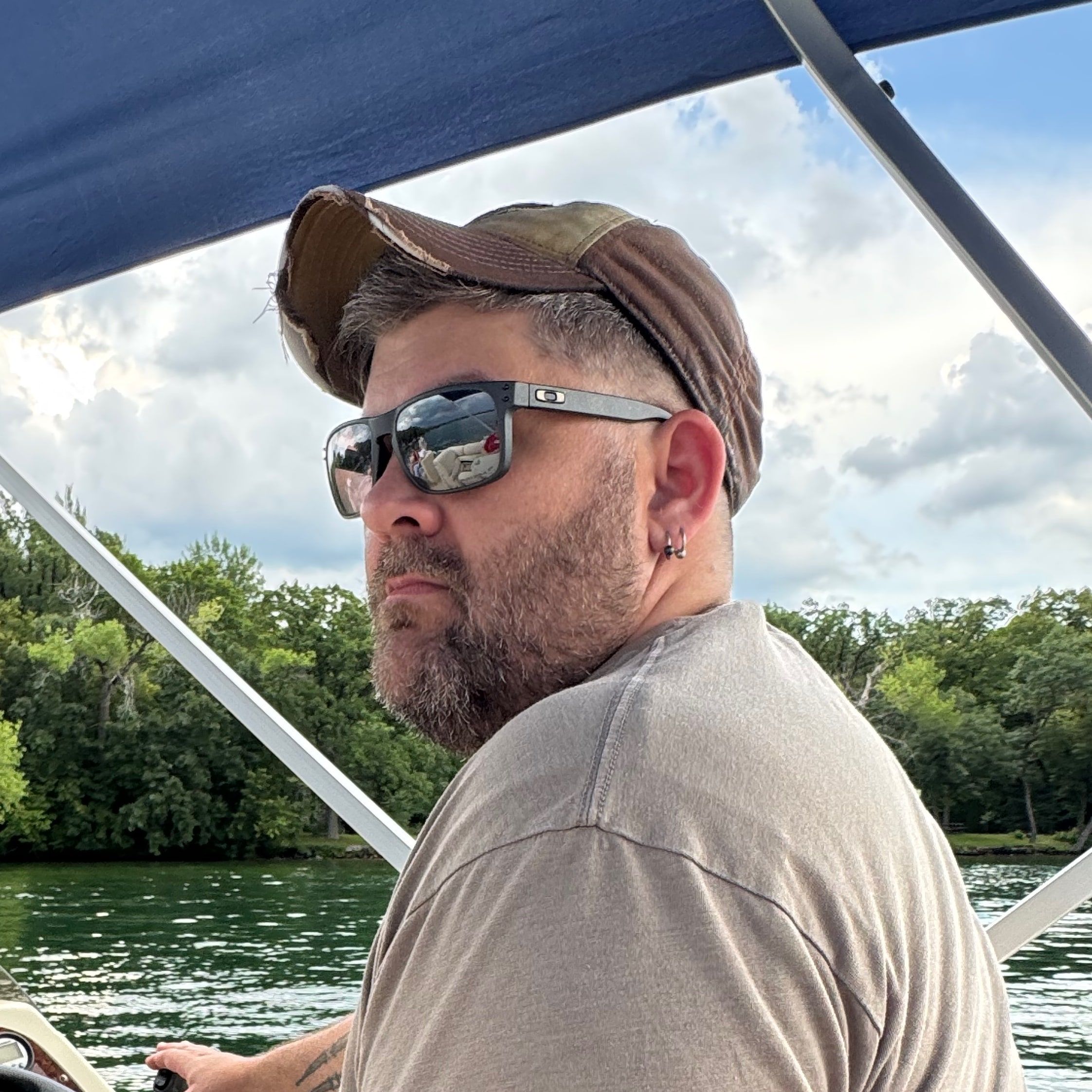 Carter Seely at the helm of a pontoon boat on a wooded Minnesota lake, looking back toward the camera