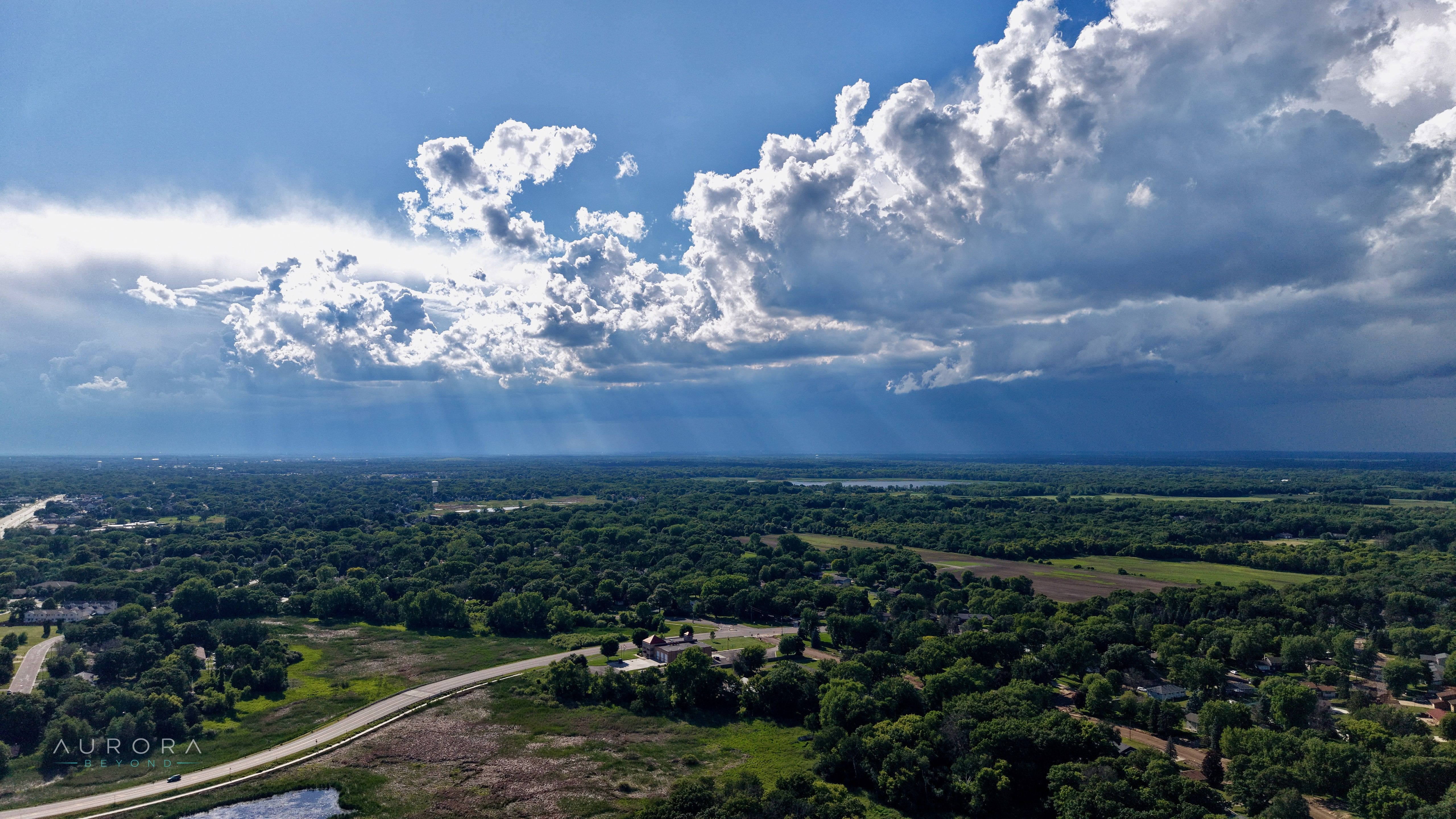 Sunbeams breaking through cumulus over green fields and a winding trail