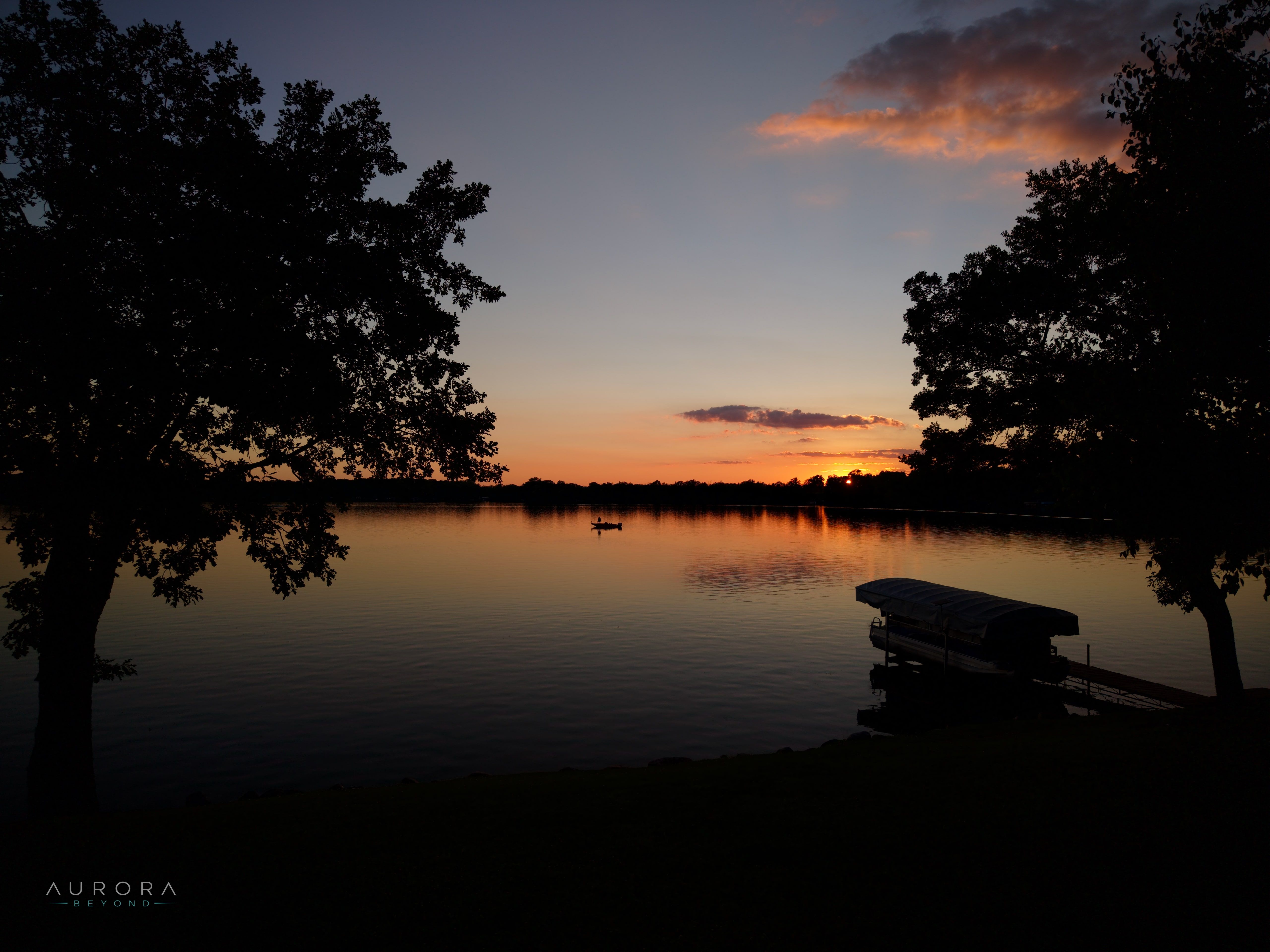 Sunset behind silhouetted trees, with a dock on still water